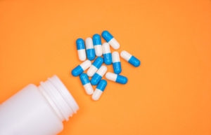 antibiotic medical drug capsule falling from bottle on orange background