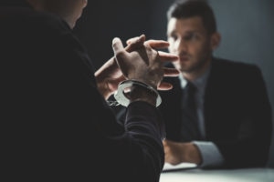 Criminal man with handcuffs being interviewed in interrogation room